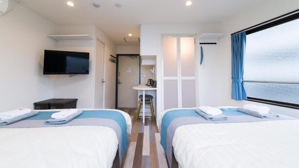 A hotel room with two beds, a TV, a small table, and a window with curtains.