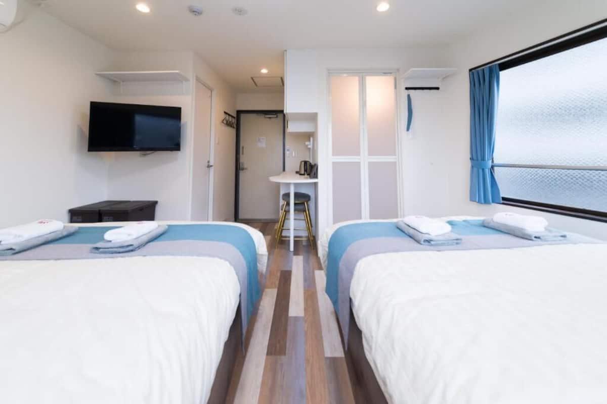 Habitación de hotel con dos camas, televisor, una mesita y ventana con cortinas.