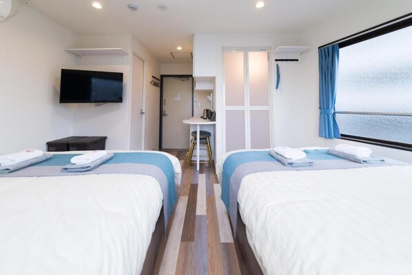 Une chambre d’hôtel avec deux lits, une télévision, une petite table et une fenêtre avec des rideaux.