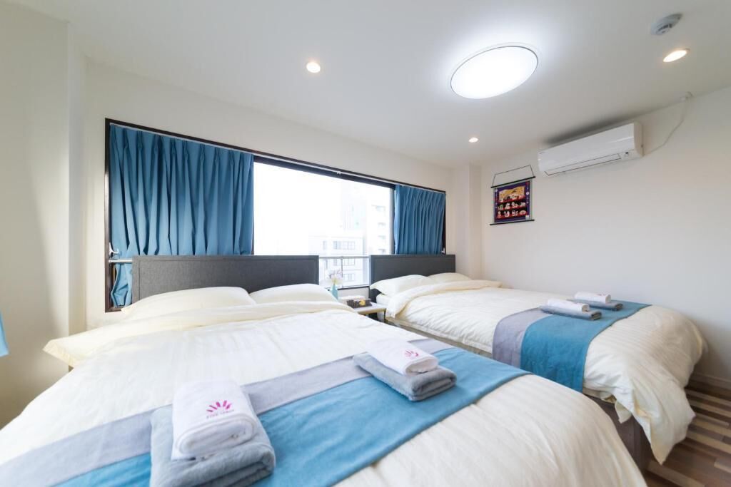 A hotel room with two beds, a large window with curtains, a nightstand, and a wall-mounted air conditioner.