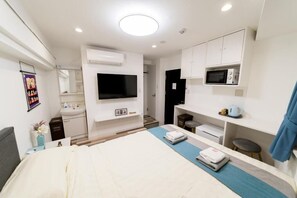 A modern hotel room with a bed, a TV, a microwave, a sink, and a small seating area. - HighFive Guest house (Toshima City)