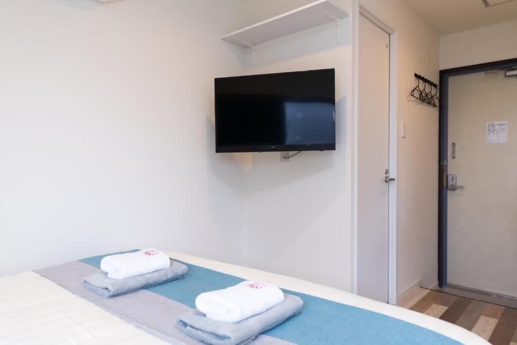 A hotel room with a bed, a flat-screen TV mounted on the wall, and a door with a coat rack.