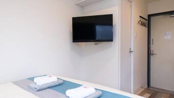 A hotel room with a bed, a flat-screen TV mounted on the wall, and a door with a coat rack.