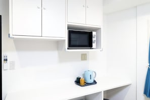 A white kitchenette with a microwave, a kettle, and a small tray with cups.