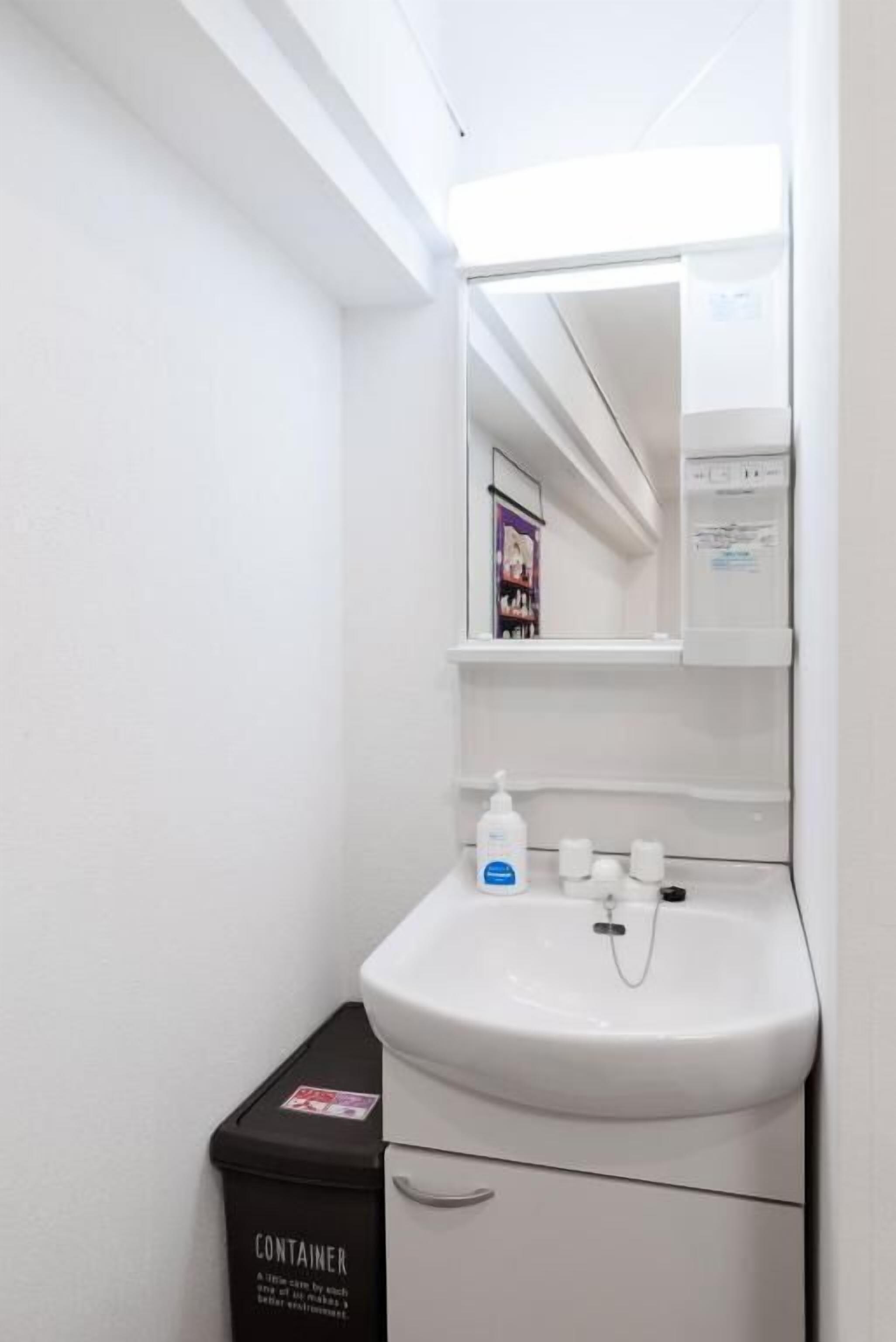 A bathroom with a white sink, mirror, and a trash bin labeled 'CONTAINER'.