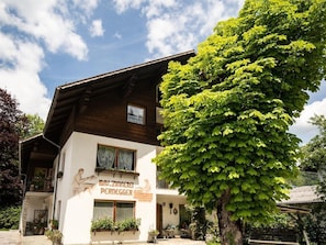 Ein Gebäude mit einem Schild, auf dem 'BAU.ZIMMER PERDEGER' steht, und ein großer Baum davor.