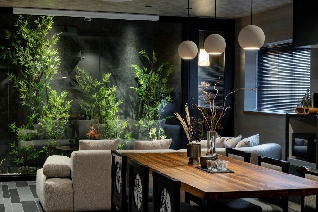 Een moderne woonkamer met een houten eettafel, comfortabele zithoek en grote potplanten.