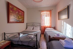 Un dormitorio con dos camas, un cuadro, una ventana con cortinas translúcidas y un cabecero de madera.
