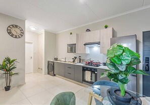 Eine moderne Küche mit Mikrowelle, Ofen und Spüle. An der Wand hängt eine Uhr und auf der Arbeitsfläche steht ein Blumentopf.