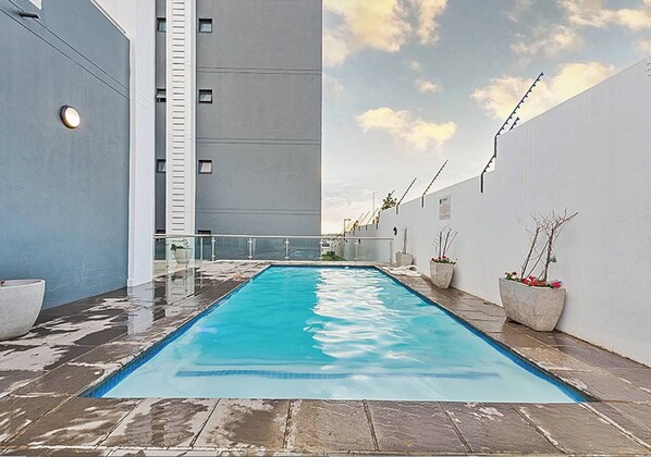 Piscina no terraço com vista ampla do céu e um edifício ao fundo.