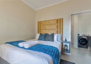 A hotel room with a bed, a nightstand, a lamp, and a washing machine. - Zalari Luxe 93 on New, 1 bed, Central & Premium Comfort (Midrand)