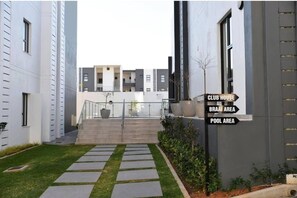 Ein modernes Gebäude mit einer Treppe, die zu einem Glasflügeldurchgang führt, mit Schildern für Clubhaus, Grillplatz und Poolbereich.
