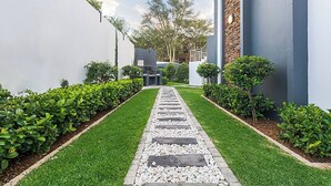 A pathway leading to a building with a modern design, surrounded by well-maintained hedges and a clear sky. - Zalari Luxe 93 on New, 1 bed, Central & Premium Comfort (Midrand)