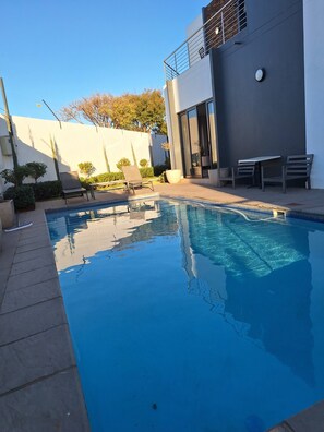 Piscina com espreguiçadeiras e um edifício moderno com varanda.