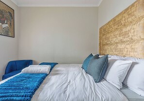 Hotellihuone, jossa on sänky, sininen tuoli ja pääty, jossa on kuvioitu pinta.