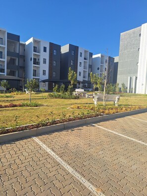 A modern apartment complex with a paved courtyard, outdoor seating, and a clear blue sky. - Zalari Luxe 93 on New, 1 bed, Central & Premium Comfort (Midrand)