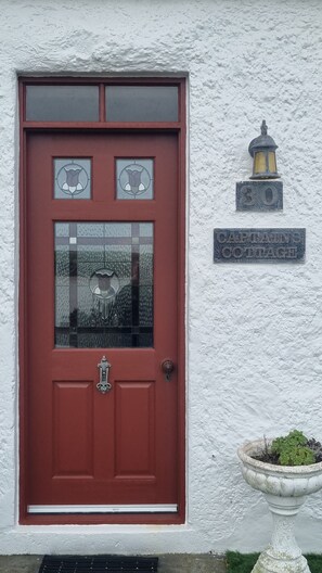 A red door with a glass panel, a lantern, and a plaque reading 'Captain's Cottage.'