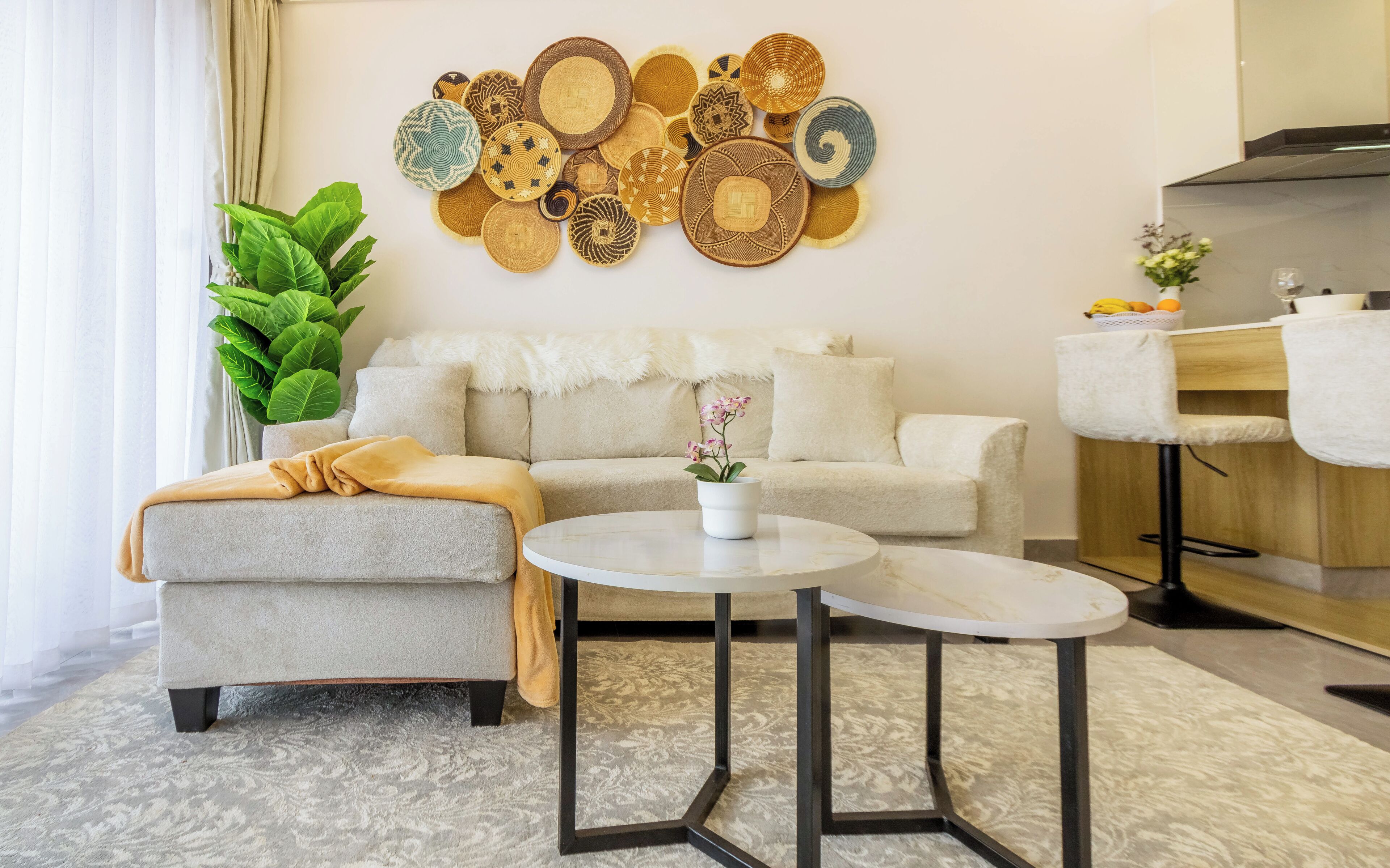A living room with a sofa, a coffee table, a wall art collection, a potted plant, and a kitchen area.