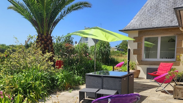 Eine Terrasse mit einem Glastisch, einem violetten Klappstuhl und einem grünen Sonnenschirm.