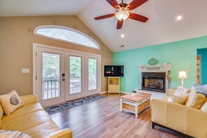 Un salon doté d’un ventilateur de plafond, d’une cheminée, d’un téléviseur et d’une grande fenêtre.
