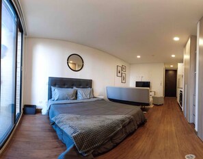 A modern bedroom with a large bed, a round mirror, a flat-screen TV, and a walk-in closet. - Modern Studio Apartment (Bogotá)