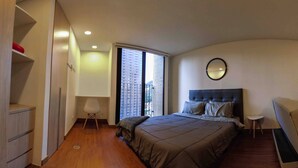 A bedroom with a bed, a bedside table, a chair, a wardrobe, and a window with a view of buildings. - Modern Studio Apartment (Bogotá)
