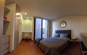 A bedroom with a bed, a bedside table, a chair, a wardrobe, and a window with a view of buildings. - Modern Studio Apartment (Bogotá)