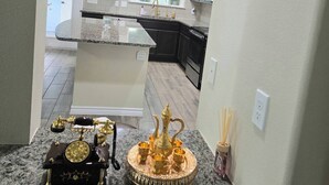 Une cuisine dotée de plans de travail en granit, d’un élément décoratif central doré et offrant une vue sur le salon attenant.