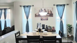 Un espace repas comprenant une table, des chaises, un lustre et des rideaux.