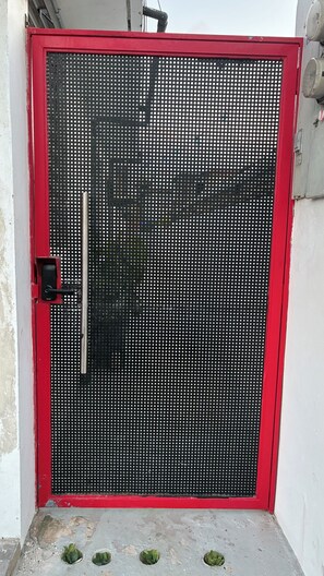 Ein rotes Metalltor mit einem Sicherheitsschloss und einer kleinen Stufe zum Betonboden.