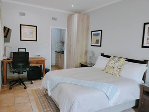 Una camera da letto con un letto, una scrivania con una sedia, un comodino e una porta che dà su un bagno.