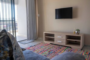 Een moderne woonkamer met een bank, een aan de muur bevestigde televisie, een houten tv-meubel en een kleurrijk vloerkleed.