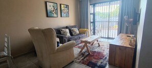 Ein Wohnzimmer mit Sofa, Sessel, Couchtisch und Blick durch ein großes Fenster.
