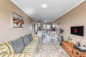 Ein Wohnzimmer mit einer Couch, einem Fernseher, einer Holzkonsole und einer Küche im Hintergrund.