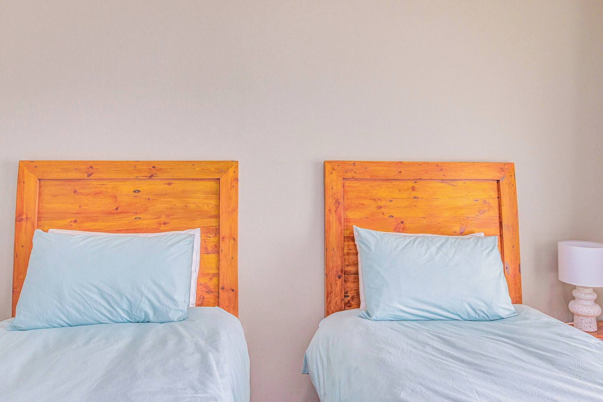Two twin beds with wooden headboards, light blue bedding, and a white lamp on a bedside table.