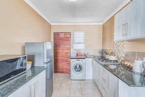 Eine kleine Küche mit Mikrowelle, Kühlschrank, Waschmaschine und Spüle.