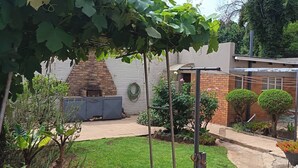 Un patio de ladrillo con una parrilla, una pérgola y un pequeño jardín con plantas en macetas y césped.