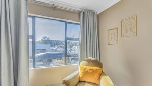 Ein Zimmer mit einem großen Fenster, einem Sessel mit Fellkissen und zwei gerahmten Wandbildern.