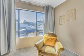 Une pièce avec une grande fenêtre, un fauteuil doté d’un coussin en fourrure et deux œuvres d’art encadrées accrochées au mur.