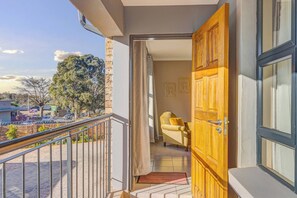 Ein Balkon mit Metallgeländer, einer Holztür und einem Stuhl in einem Zimmer.