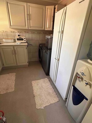 A compact kitchen with white cabinets, a microwave, a washing machine, and a refrigerator. - Kalista’s house Villa (Roodepoort)