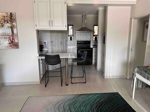 A modern kitchen with white cabinets, a black stove, and a dining area with two chairs. - Kalista’s house Villa (Roodepoort)