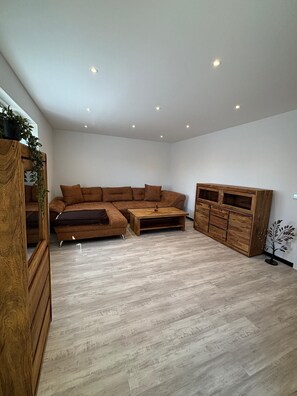 Un salon moderne avec un canapé d’angle, un meuble en bois et des spots encastrés au plafond.