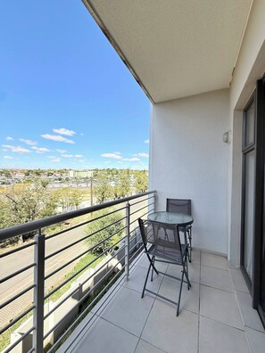 Ein Balkon mit Tisch und Stühlen, Blick auf eine Stadtlandschaft und ein klarer Himmel.