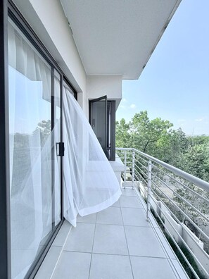 Ein Balkon mit weißem Vorhang, einer Schiebeglastür und einem Metallgeländer.