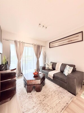 Ein modernes Wohnzimmer mit einem dunkelbraunen Sofa, einem Holztisch und einem großen Fenster mit Vorhängen.