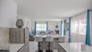Una cocina moderna con una isla central, taburetes de bar y un comedor con sofá y sillas.