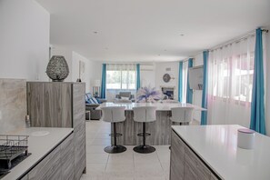 A modern kitchen with a central island, bar stools, and a dining area with a sofa and chairs. - A Casa Serena: The soul of Corsica in a picturesque setting... (Santa-Maria-Poggio)
