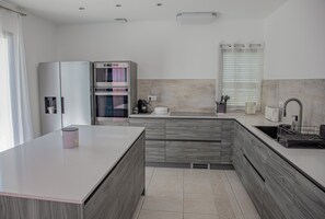 A modern kitchen with a central island, built-in oven, and a sink with a window above. - A Casa Serena: The soul of Corsica in a picturesque setting... (Santa-Maria-Poggio)