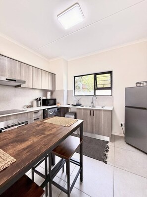 A modern kitchen with a wooden dining table, stainless steel appliances, and a window with a view.